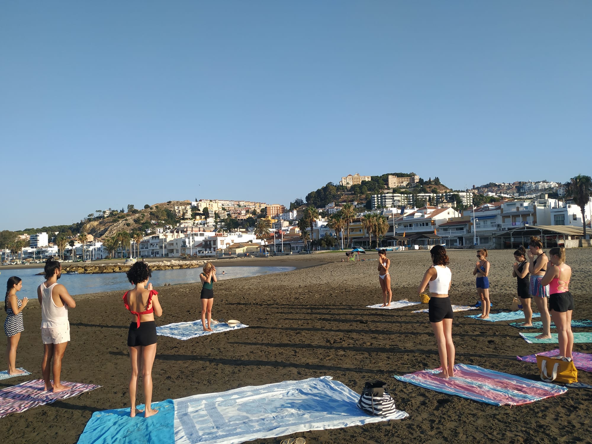 Grupo de mujeres practicando yoga en la playa de Málaga al amanecer, despedida de soltera con Violeta Yoga
